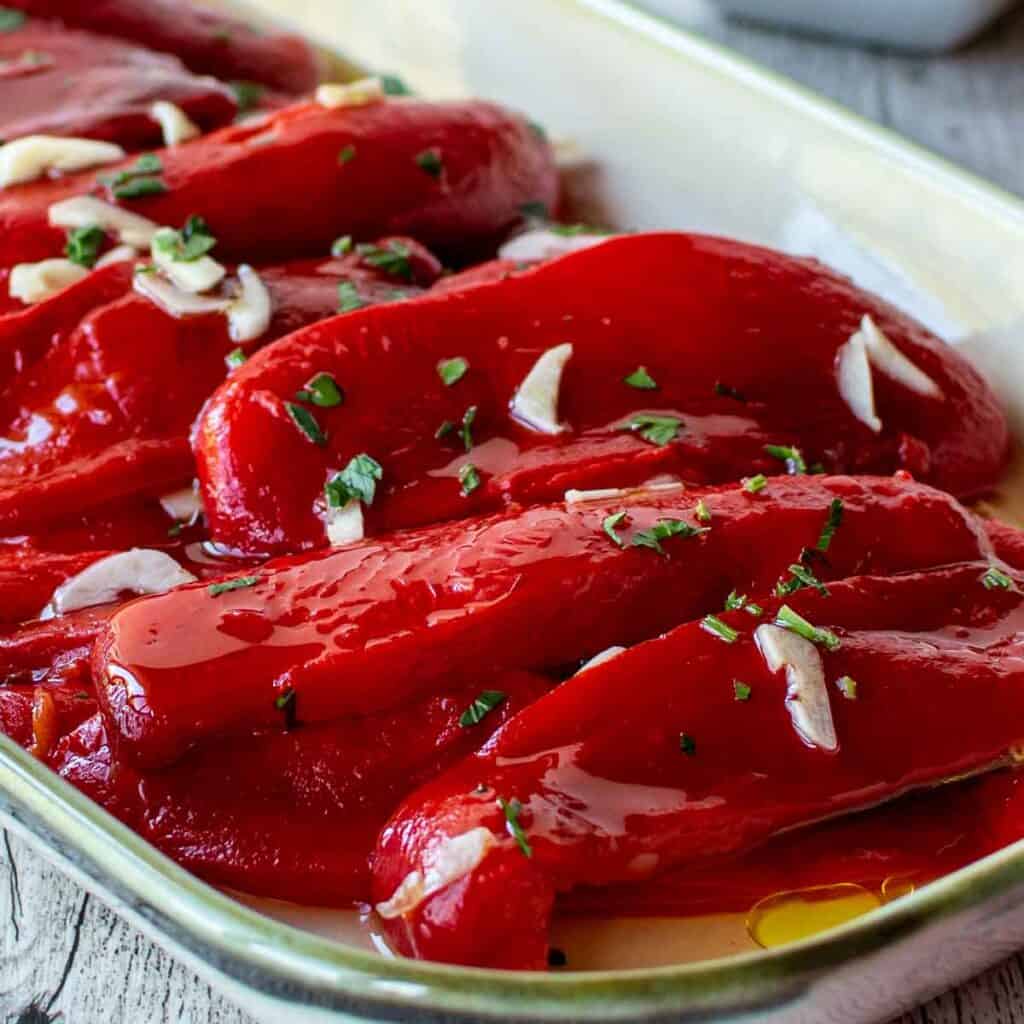 Italian Roasted Peppers on an oblong dish with slivers of fresh garlic and chopped parsley scattered on top.