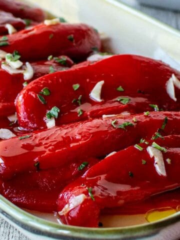Italian Roasted Peppers on an oblong dish with slivers of fresh garlic and chopped parsley scattered on top.