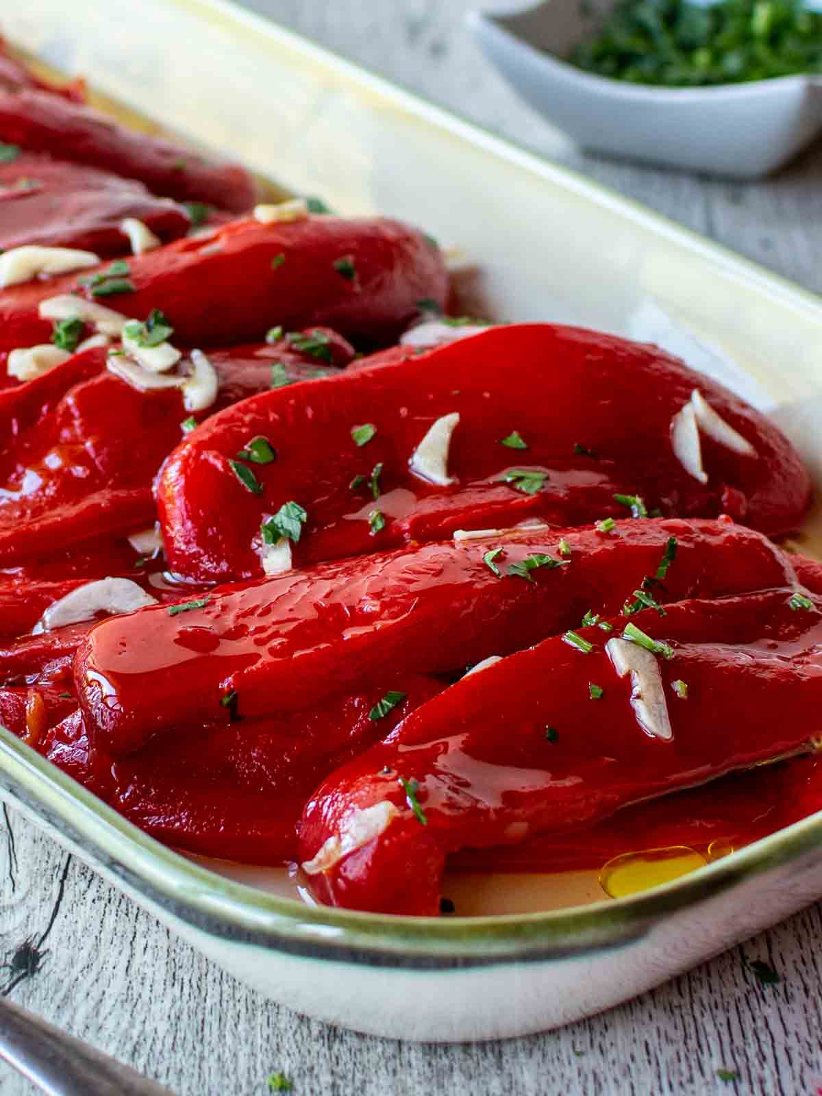 Italian Roasted Peppers on an oblong dish with slivers of fresh garlic and chopped parsley scattered on top.