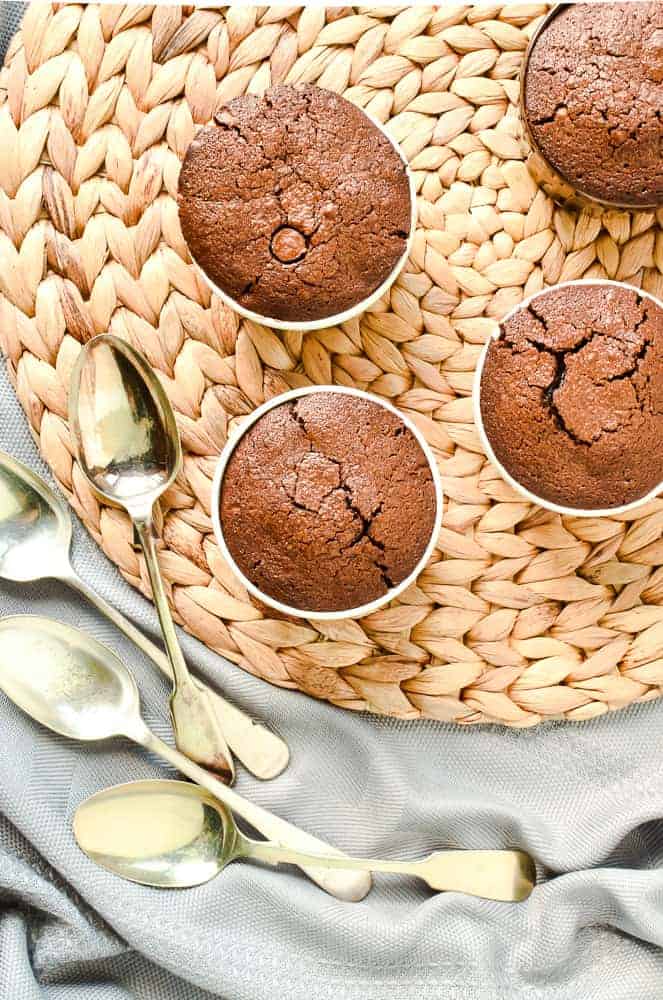 Four baked chocolate puddings, with spoons on a raffia mat viewed from above