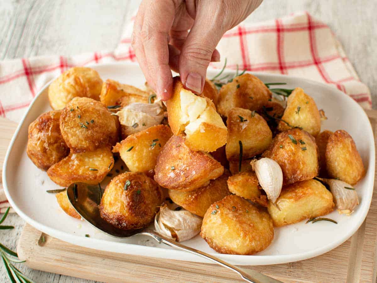 Close up of roasted potatoes with one picked up and broken open. 