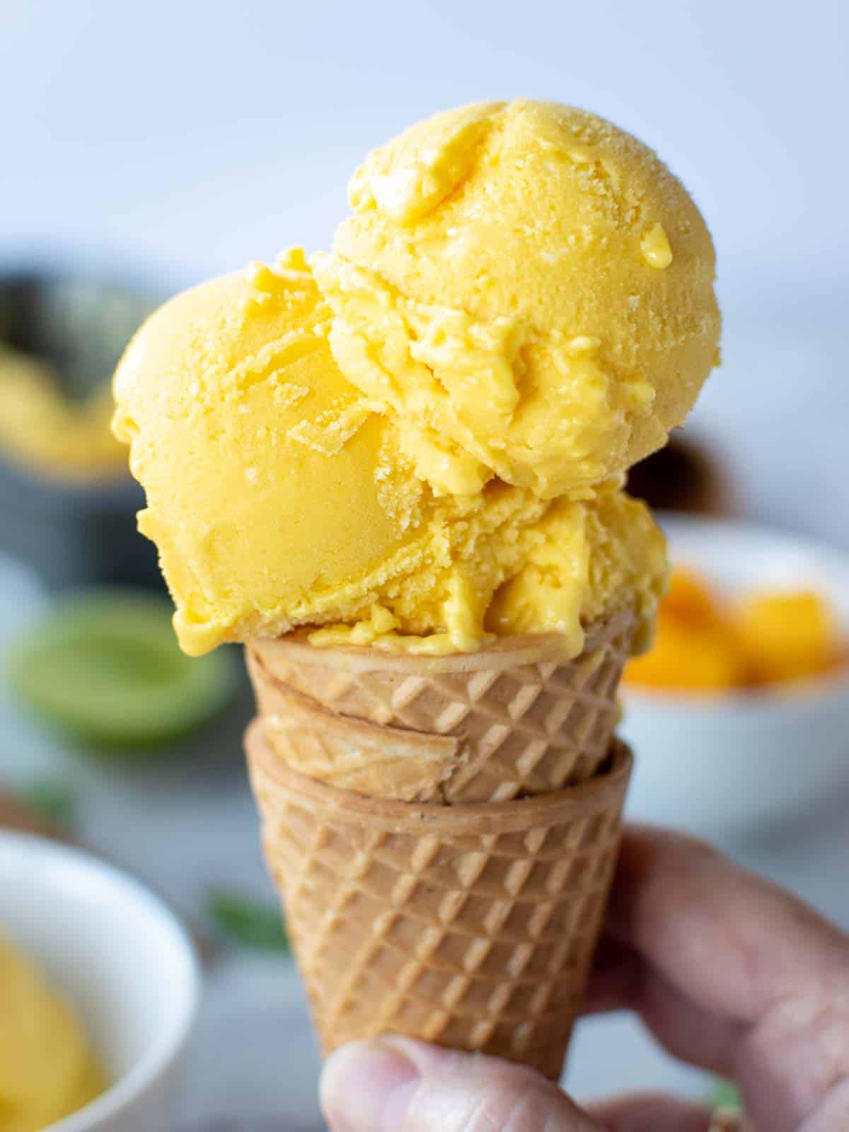 Close up of 3 scoops of mango ice cream in a cone.