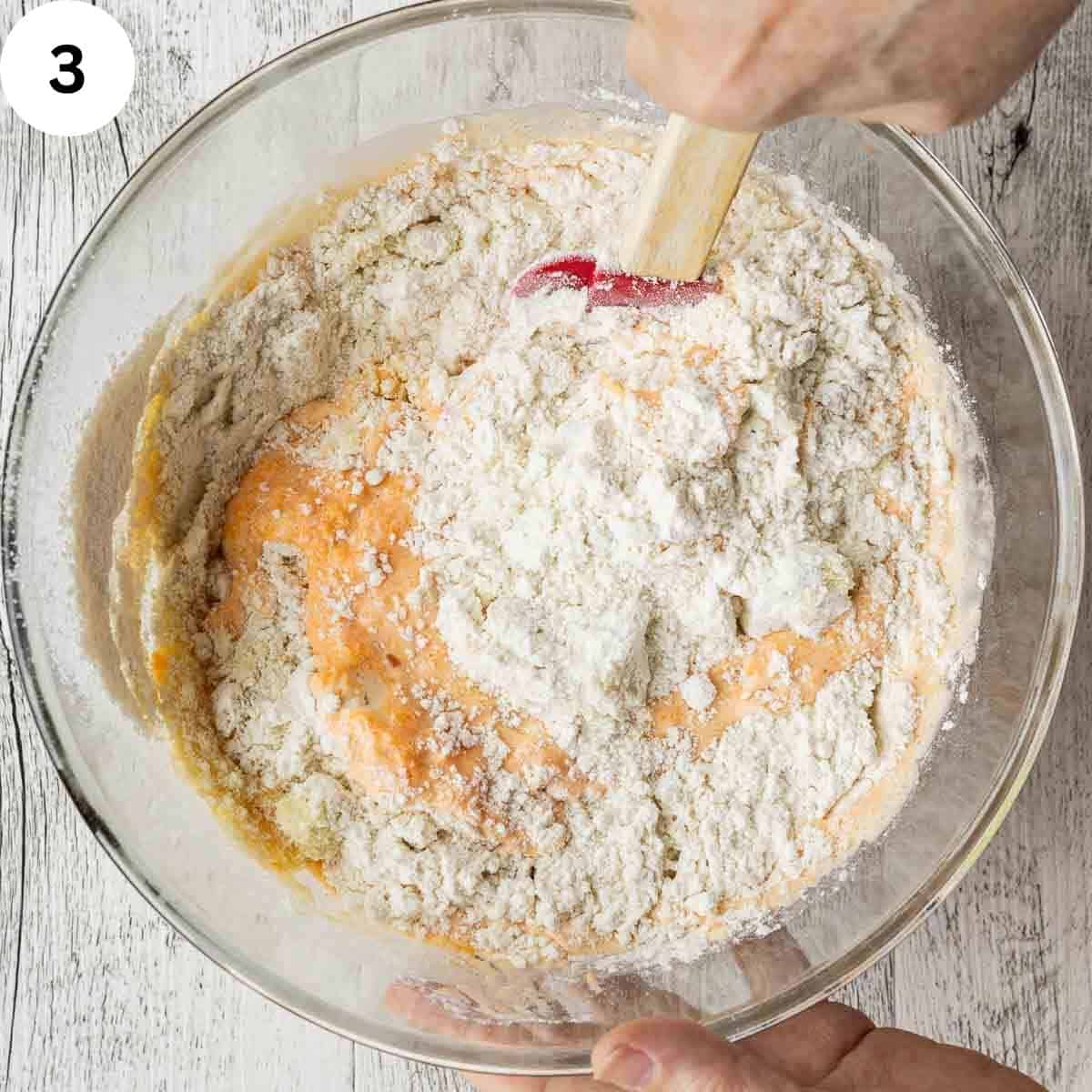 Stirring flour into orange, thick mixture to make cake batter.