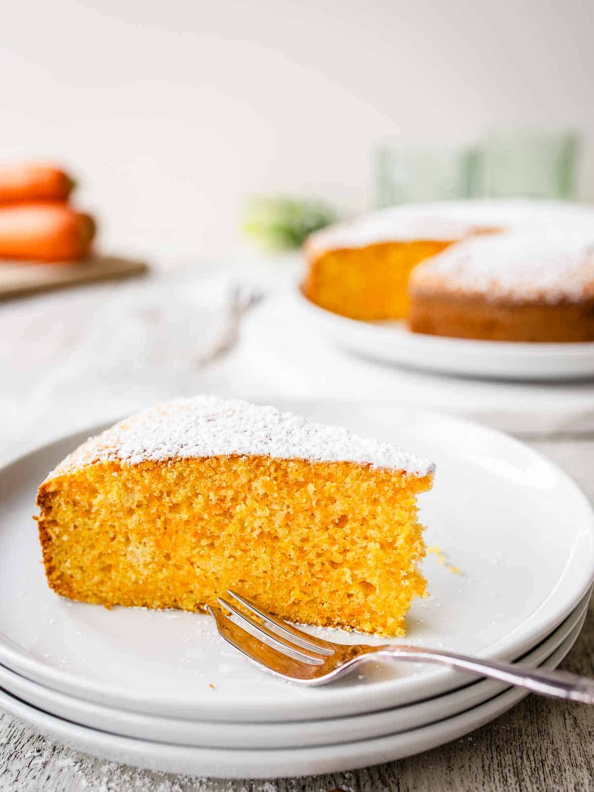 Wedge of Italian carrot cake on three stacked white plates.