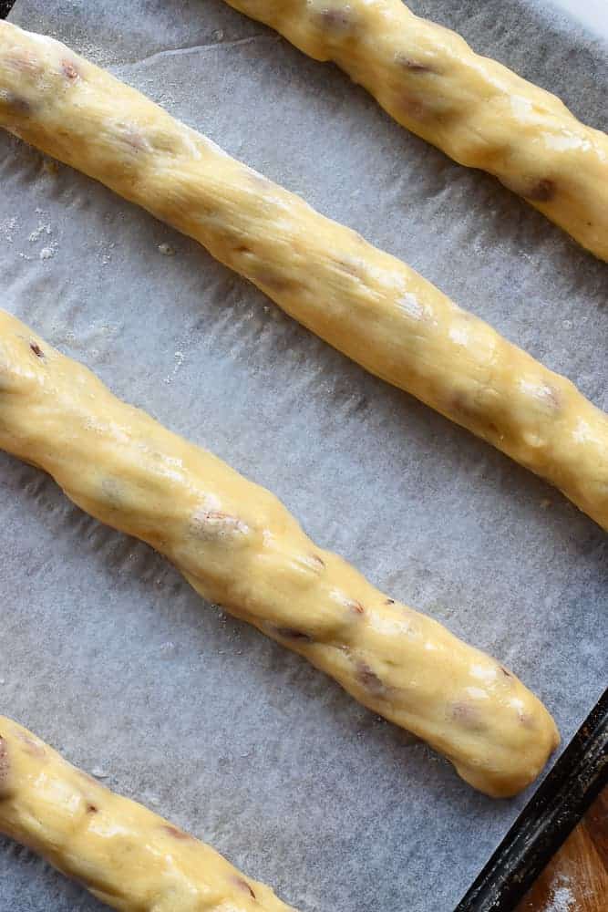 four uncooked logs of dough on baking paper viewed from above.