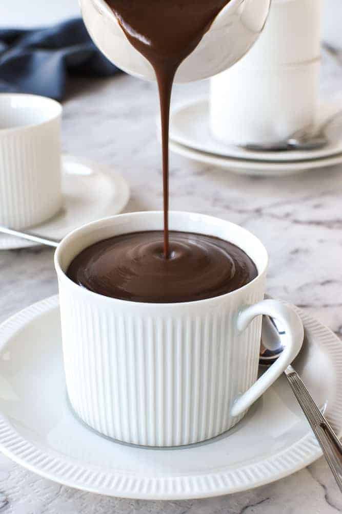 white cup and saucer being filled with Italian hot chocolate poured from a white jug.