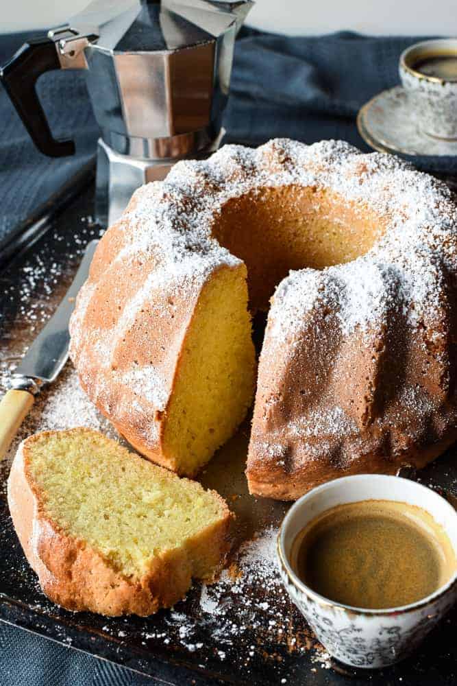 Lemon Yogurt cake with slice in the front and two espresso cups of coffee and moka pot.