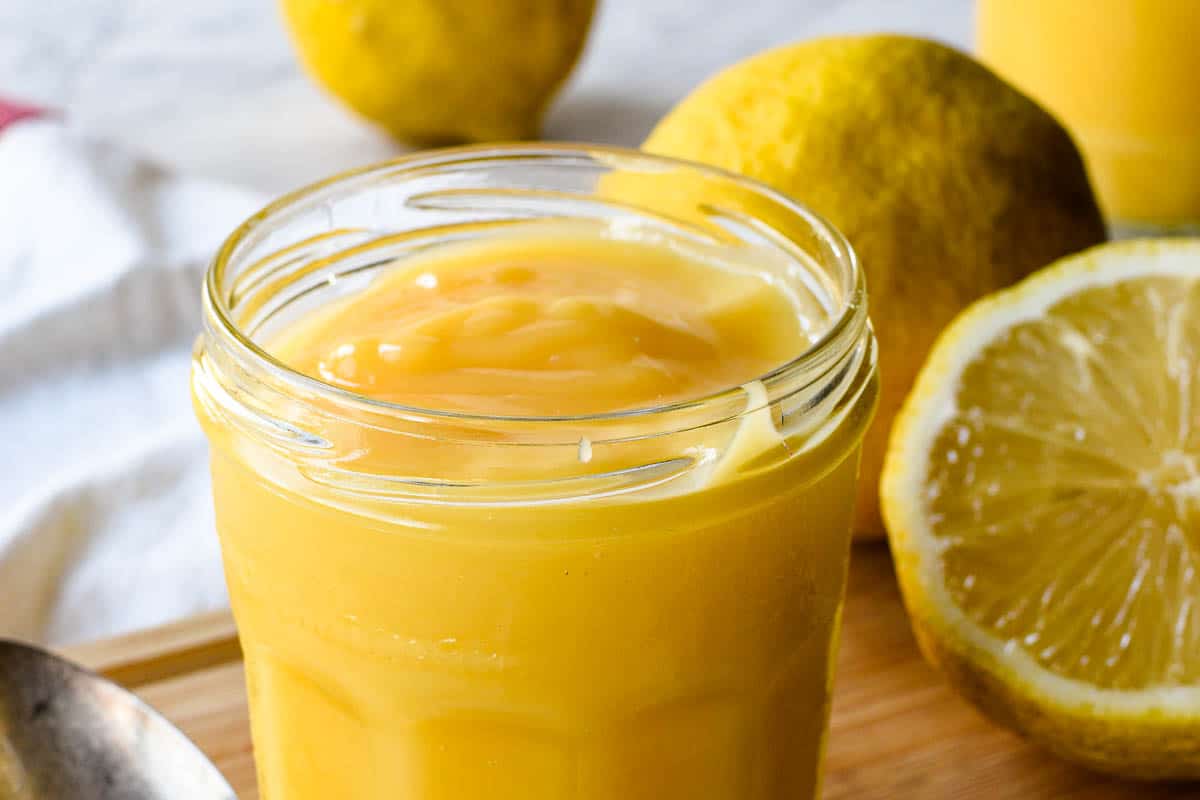 A close up of the homemade curd in a glass jar on a wooden cutting board. 