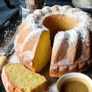 Lemon Yogurt cake with slice in the front and two espresso cups of coffee and moka pot.