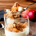 glass of panna cotta with apple crumble topping and a spoonful being removed with text on photo