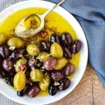 white plate with assorted olives in olive oil and a spoon viewed from above
