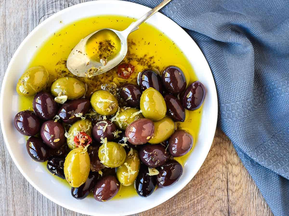 white plate with assorted olives in olive oil and a spoon viewed from above.