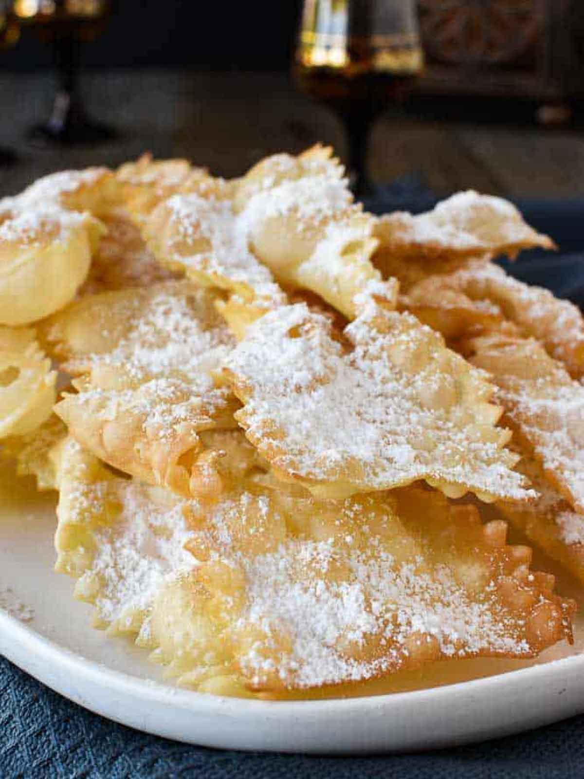 Crostoli are a crispy fried Italian pastry which are popular during Carnevale and many other celebrations. Try stopping at just one - impossible! #crostoli #angelwings #Italianfritters #easter #christmasrecipes #lent #Italiancookie #italianrecipes Crostoli dusted with powdered sugar viewed from the front.