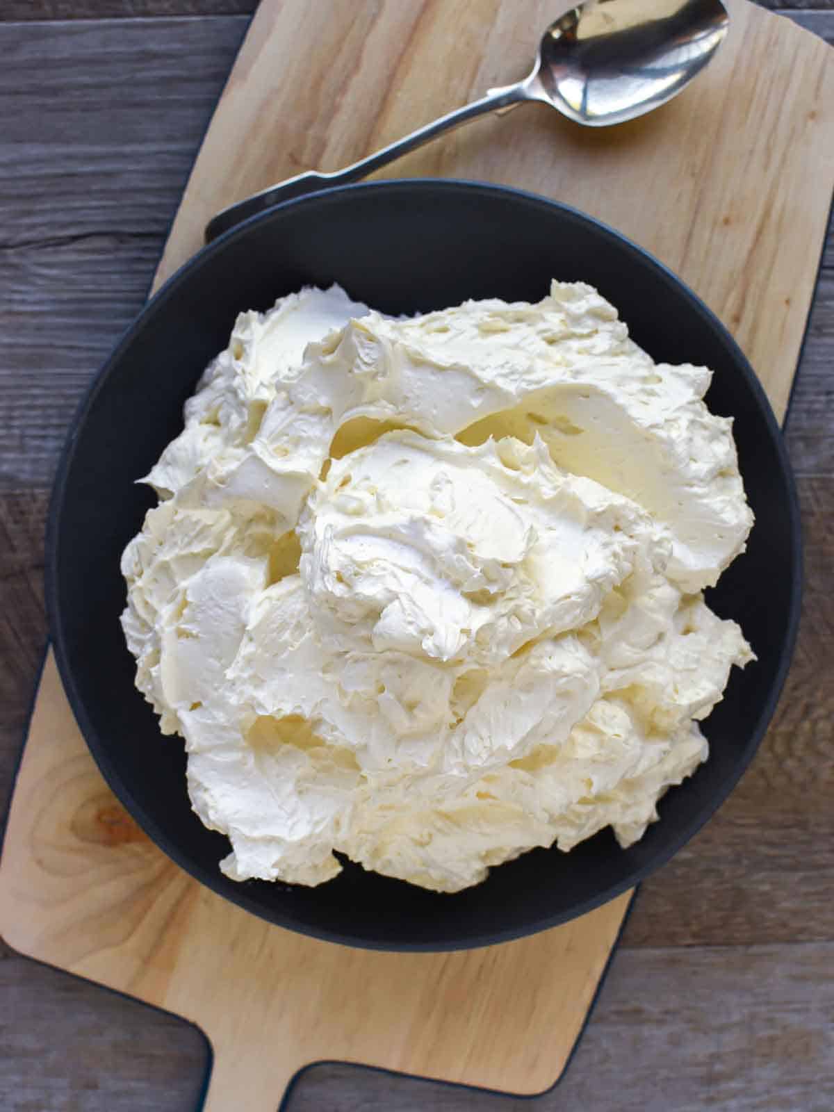 Thick creamy buttercream in black bowl viewed from above.