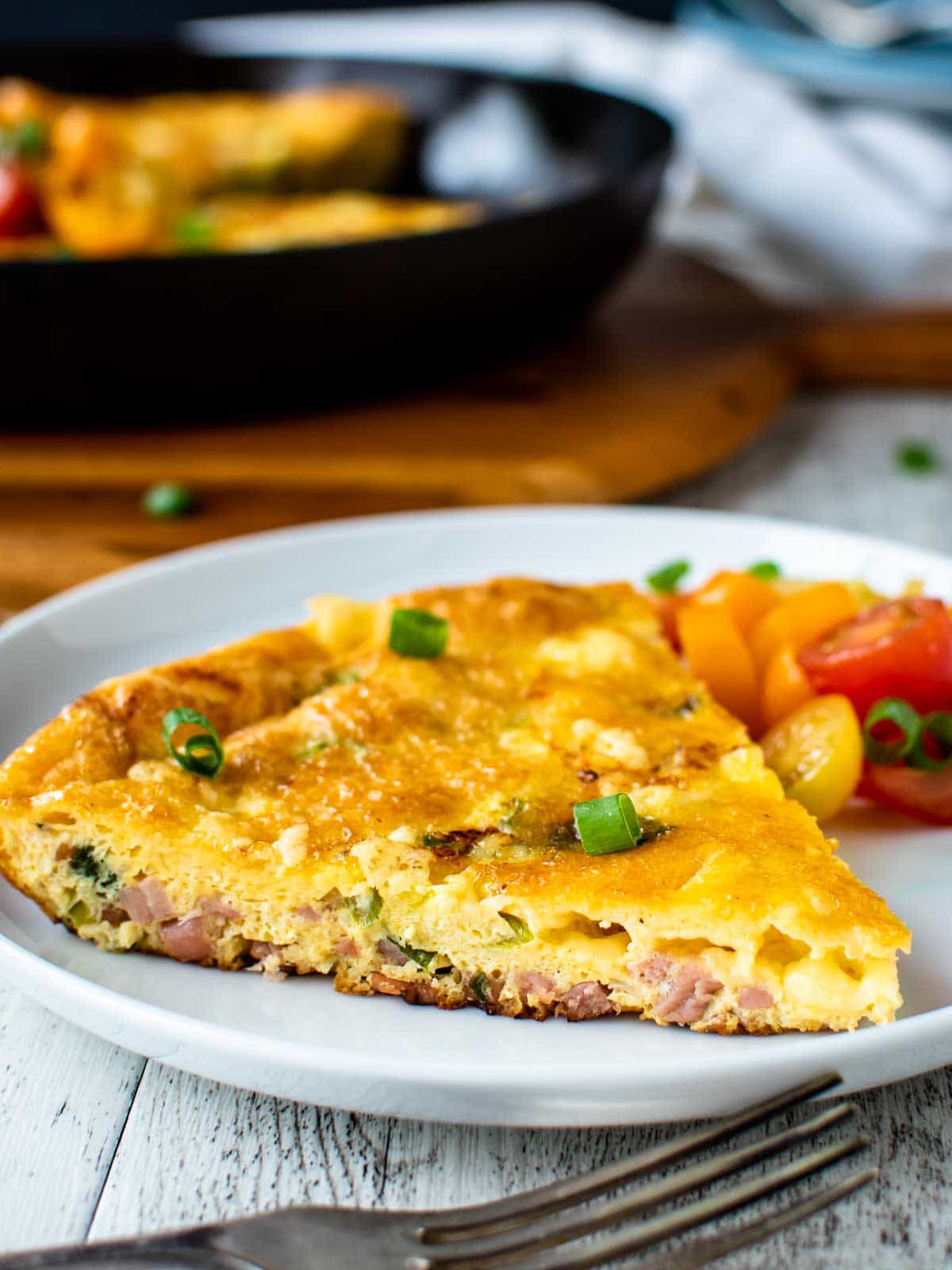 Wedge of frittata with ham and cheese on a white plate.