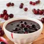 Cherry sauce in white bowl with cherries scattered around, spoonful of sauce beside bowl