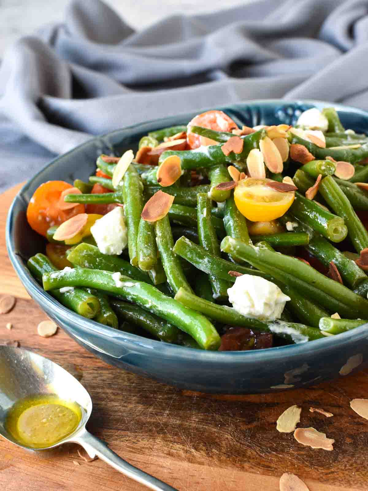 Green bean salad with tomatoes and feta in a blue bowl.