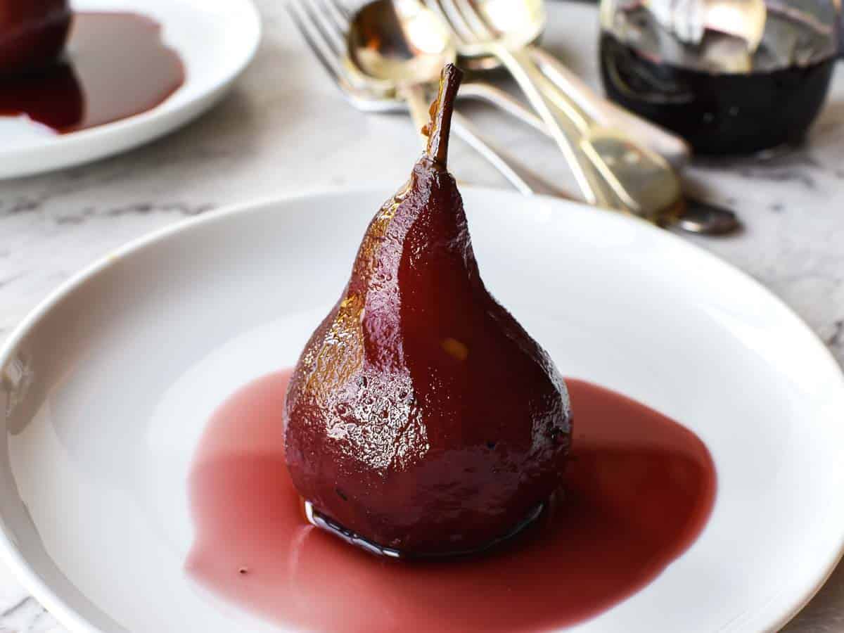 A poached pear sitting upright in red syrup on a white plate