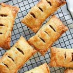 Image with text - image is 8 puff pastry apple turnovers on a black wire rack viewed from above