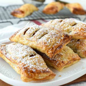puff pastry apple turnovers on a white plate dusting with powdered sugar
