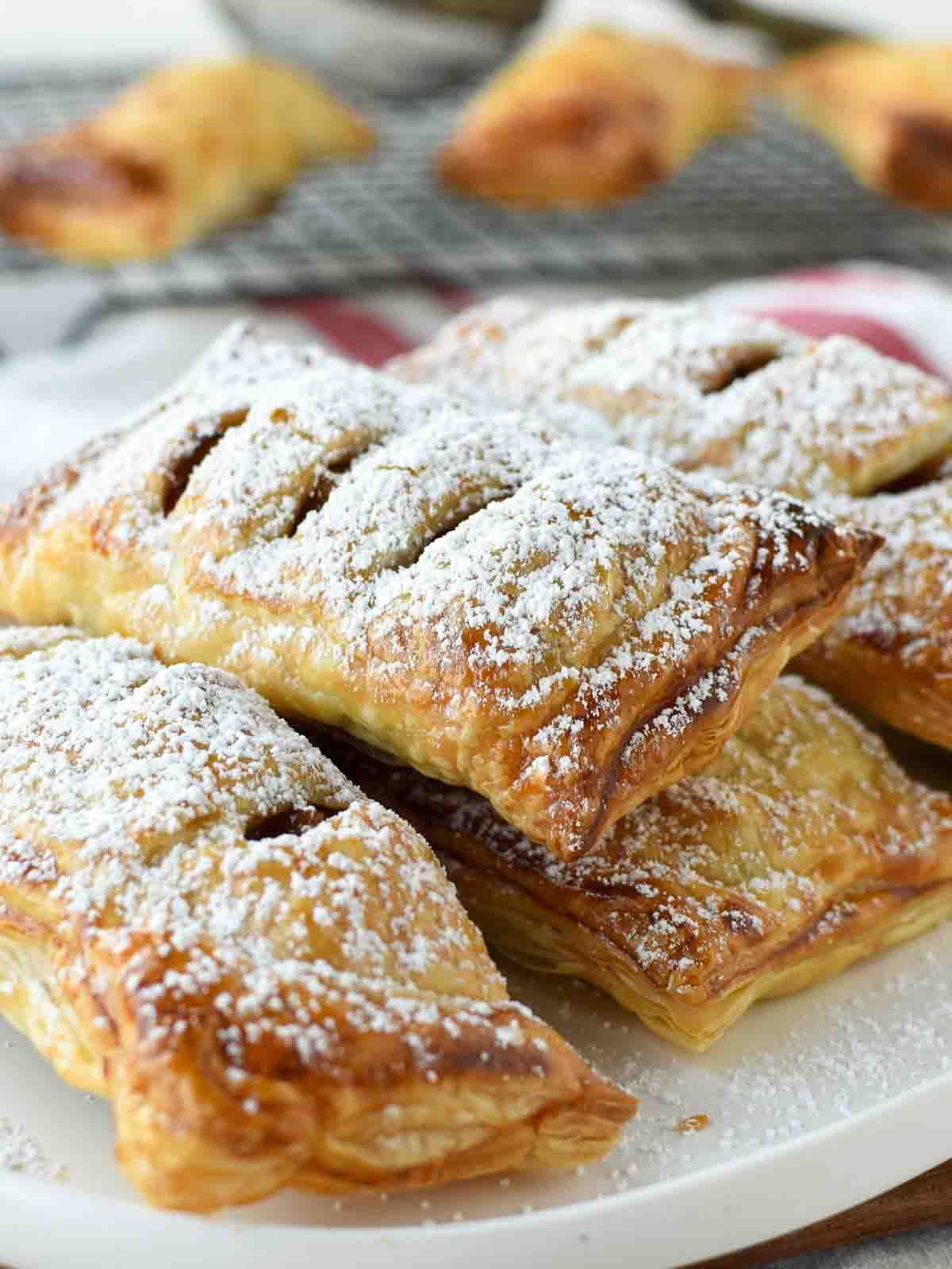 puff pastry apple turnovers on a white plate dusting with powdered sugar.