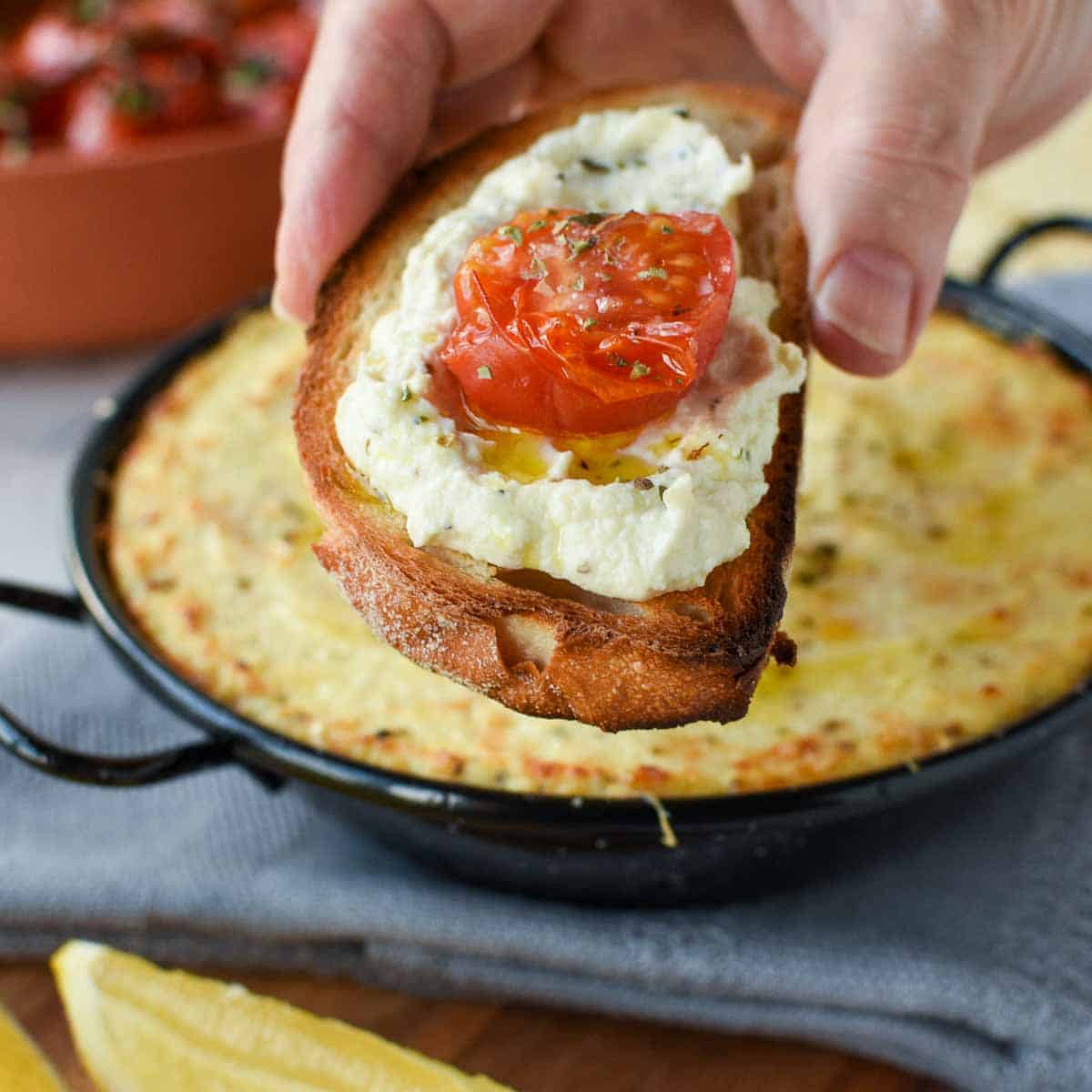 slice of toasted bread spread with baked ricotta and topped with half a slice of roasted cherry tomato