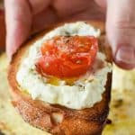 slice of toasted bread spread with baked ricotta and topped with half a slice of roasted cherry tomato