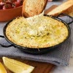 baked ricotta in black enamel pan on grey cloth with a slice of toasted bread dipping in