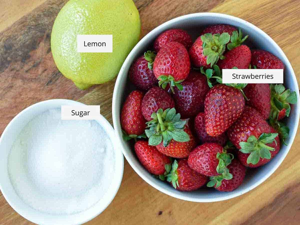 a lemon, a bowl of strawberries and a bowl of white sugar