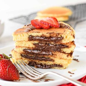 five stacked nutella filled pancakes on white plate sliced in half showing the nutella oozing out