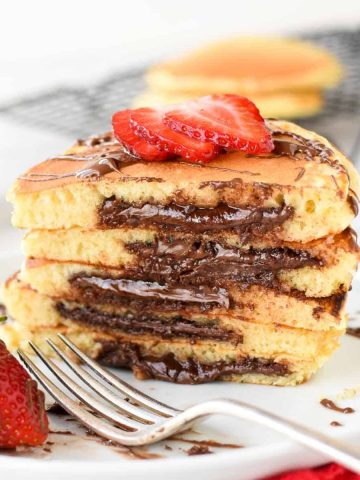five stacked nutella filled pancakes on white plate sliced in half showing the nutella oozing out