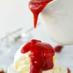 glass bowl of vanilla ice cream with strawberry coulis poured over from a white jug