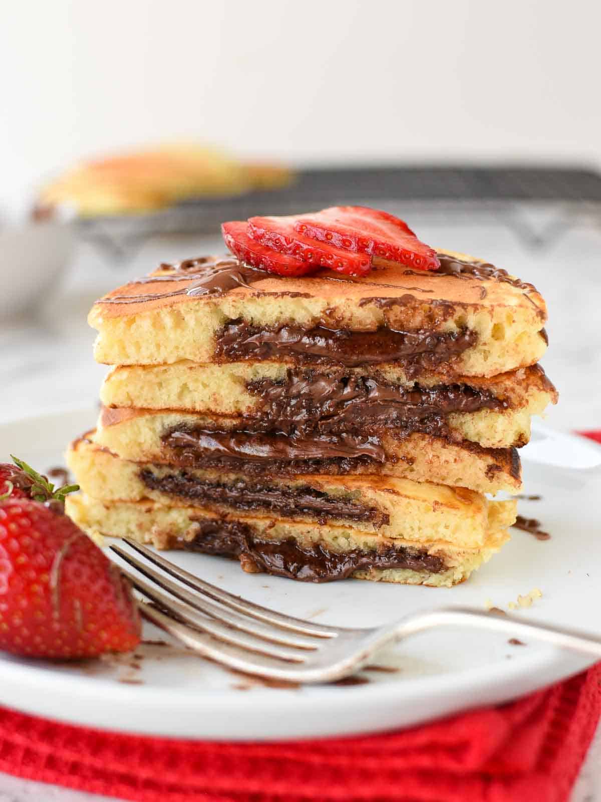 Nutella pancakes cut in half and stacked on a white plate.