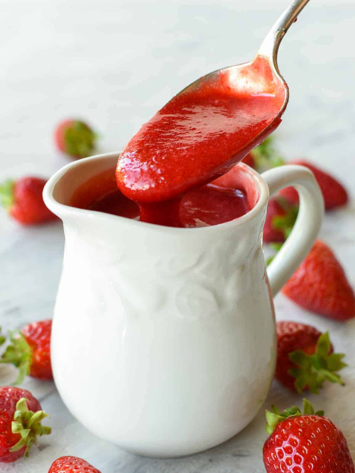 a spoon full of strawberry sauce being poured into a white jug.
