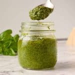 glass jar of basil pesto with a spoonful being spooned out, fresh basil in the background
