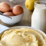 Image with text. Text reads Italian Pastry Cream Smooth and Delicious. Image is white bowl of pastry cream on pale blue cloth with bottle of milk, a lemon, eggs and a vanilla bean in the background