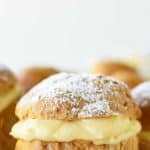 Image with text which read Italian cream puffs with pastry cream filling; image is pastries filled with custard on black wire rack viewed from front on