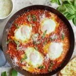 four poached eggs in tomato sauce in black pan viewed from above