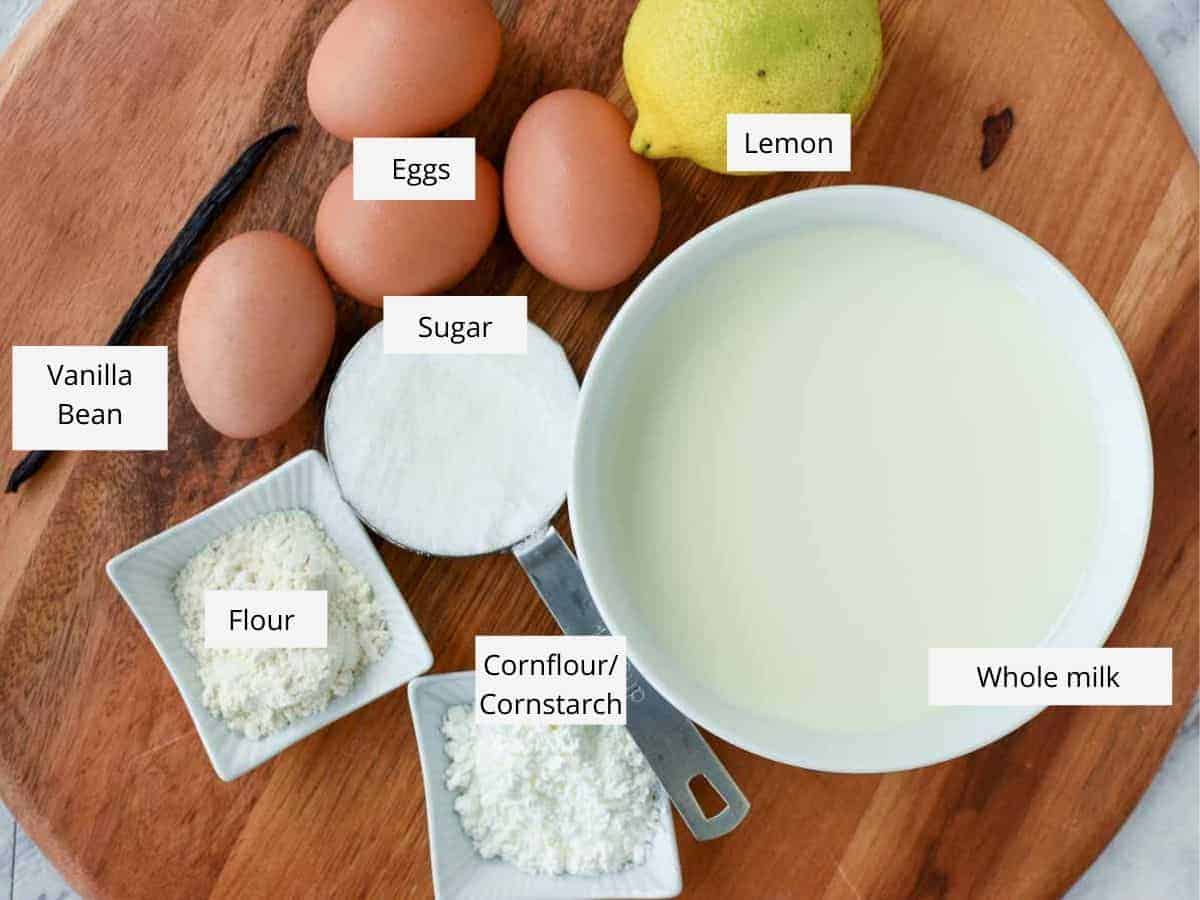 Ingredients viewed from above - eggs, lemon, milk, sugar, flour, cornflour/cornstarch, vanilla bean.