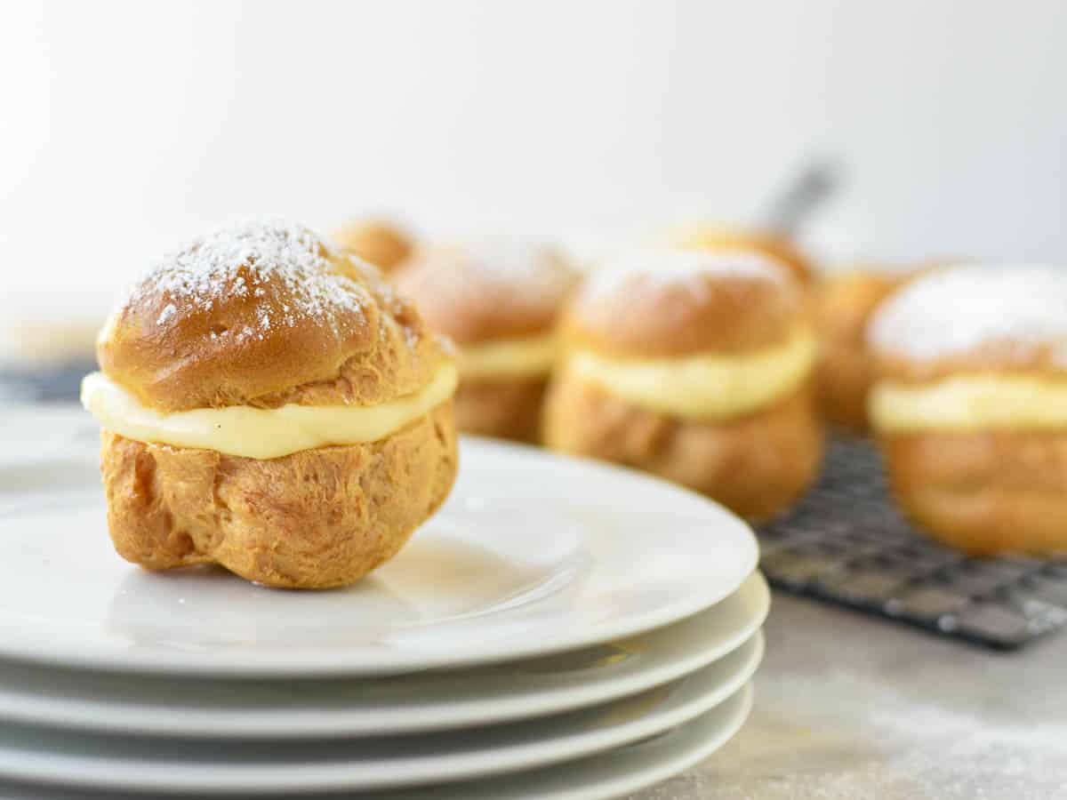 cream puff filled with custard on stack of white plates and more cream puffs in the background