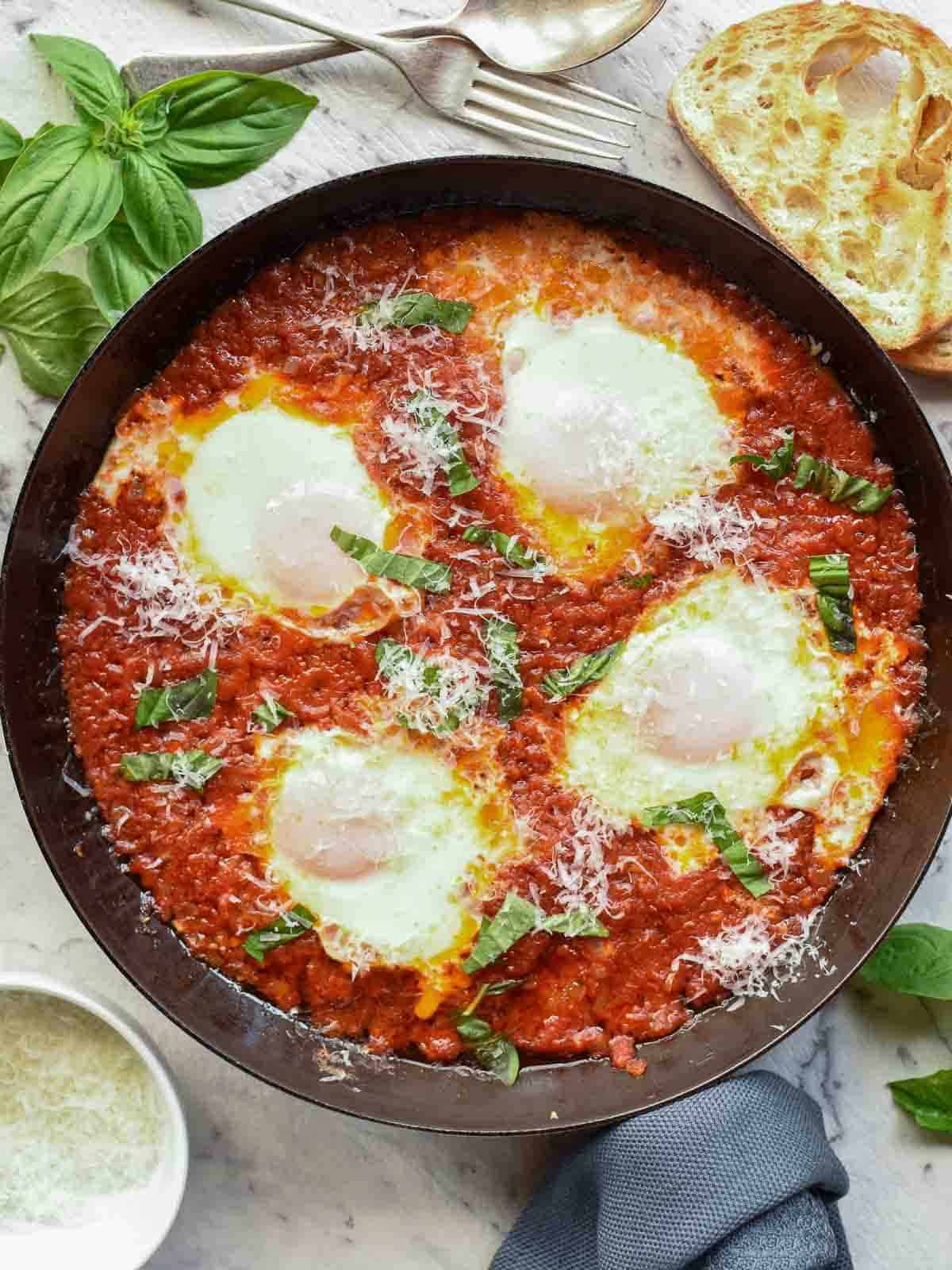 four poached eggs in tomato sauce in black pan viewed from above.