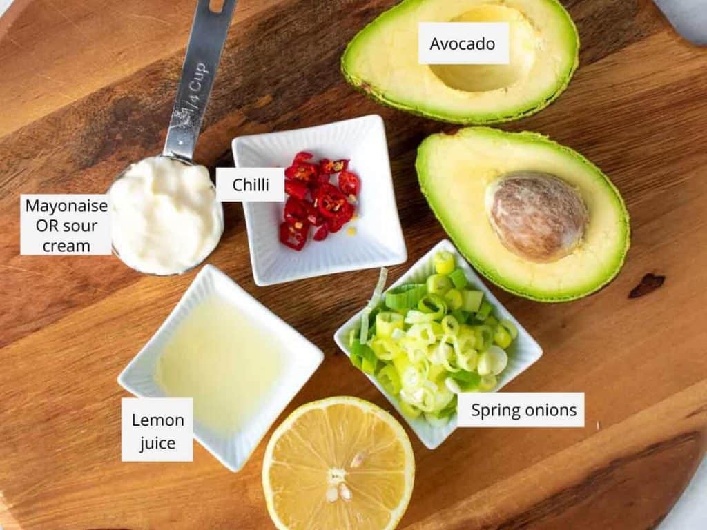 avocado cut in half with cut side up, chopped spring onions, half lemon, lemon juice, mayonaise, chopped red chilli all on wooden board and named
