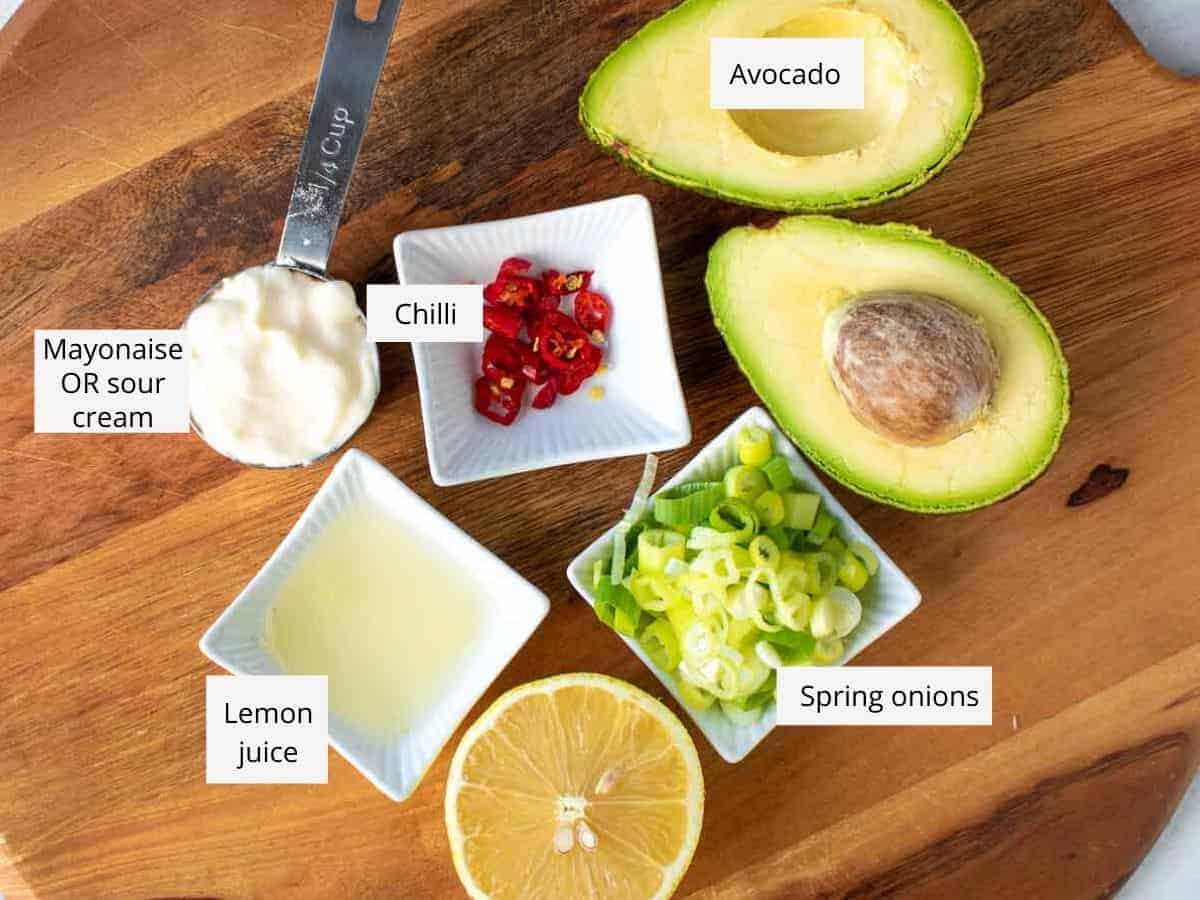 avocado cut in half with cut side up, chopped spring onions, half lemon, lemon juice, mayonaise, chopped red chilli all on wooden board and named