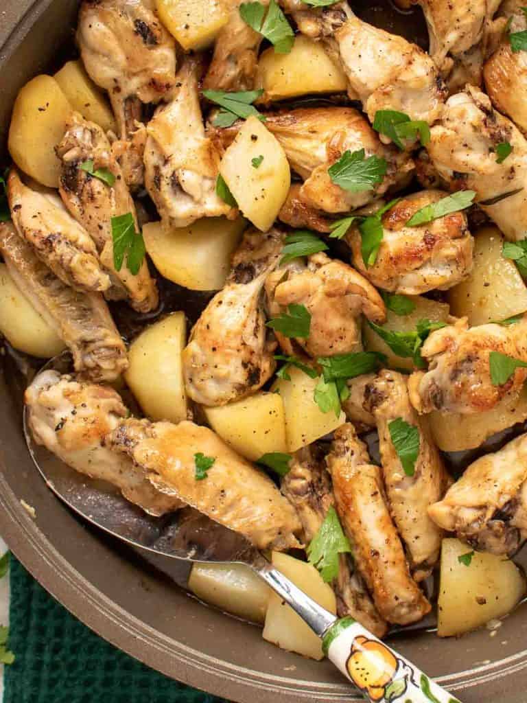 close up of braised chicken wings with potato chunks sprinkled with chopped parsley viewed from above