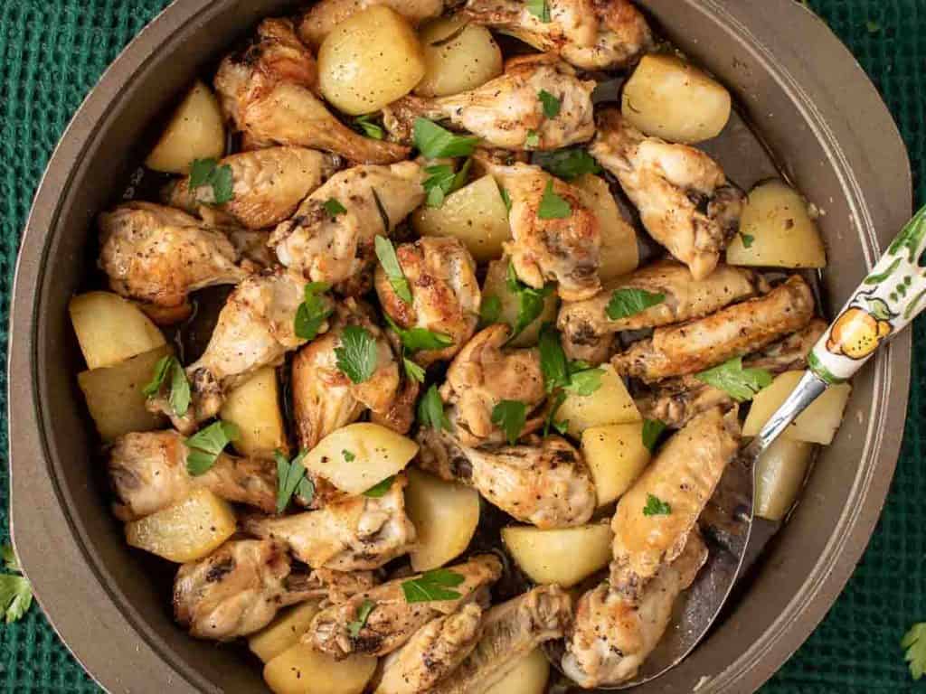 braised chicken wings with potato chunks sprinkled with chopped parsley viewed from above