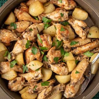 braised chicken wings with potato chunks sprinkled with chopped parsley viewed from above