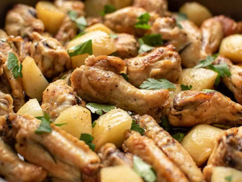 close up of braised chicken wings with potato chunks sprinkled with chopped parsley viewed from a 45 degree angle