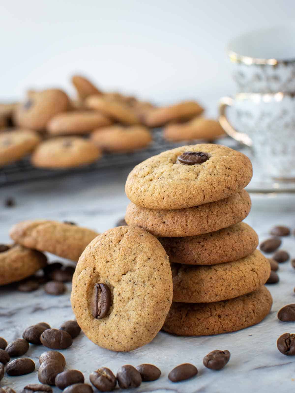 five coffee cookies stacked with a sixth cookies leaning on the stack - cookies in the background and coffee beans scattered around.