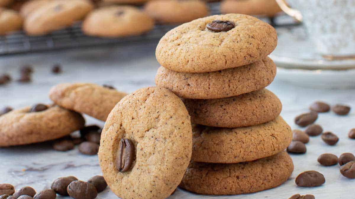 stack of five cookies with a 6th cookies leaning against the stack and more cookies and coffee beans around.