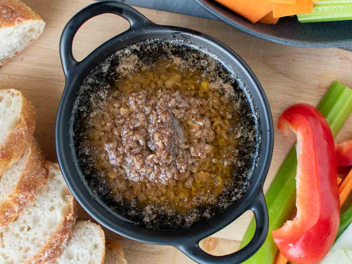 The finished recipe in a black bowl surrounded by sliced vegetables and bread viewed from above.